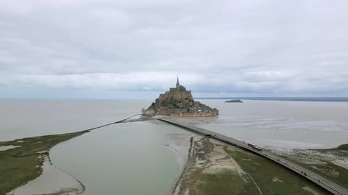 People walking along bridge of Mont Saint Michel during low tide on cloudy day, Normandy in France.