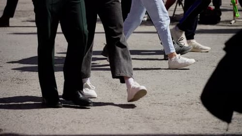 Dynamische Flachwinkelaufnahme verschiedener Füße in Bewegung auf einer Stadtstraße mit einer Reihe von Schuhen und