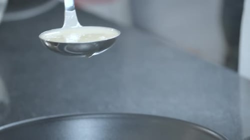 Close up view of batter being poured into hot frypan for making pancakes.