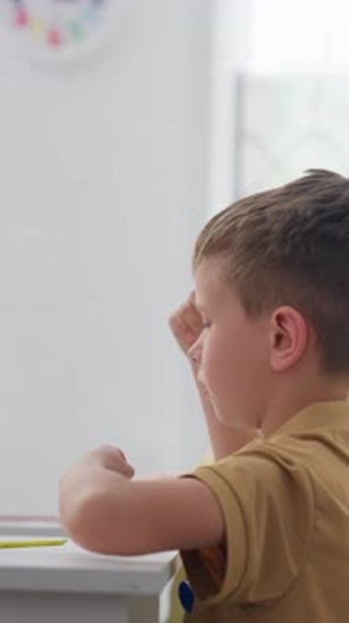 Young Boy in Tan Polo Pointing Across a Table in Softly Lit Interior