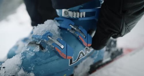 Close up of a blue ski boot on snow, with hand in black glove tightening the boot.