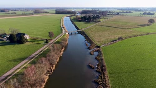 High-angle shot of a rural landscape featuring a bridge crossing a straight river The scene includes