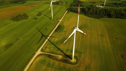 Drone shot of a few wind turbines working and generating green electric energy on a green field on a