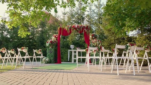 Wedding arch at the restaurant with red flowers and wooden chairs.