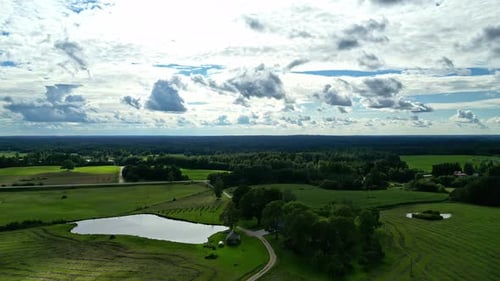 Aerial view of cumulus clouds on sky with rural green field filled with lush trees and bushes during