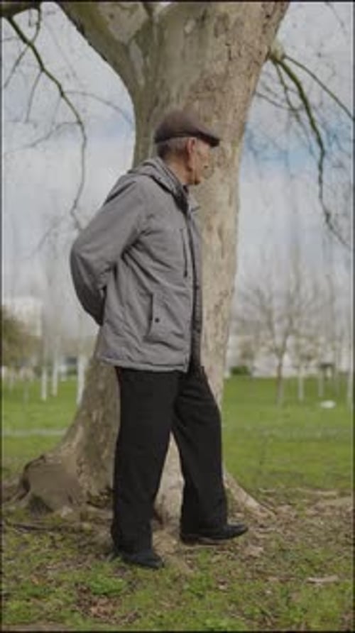 Elderly Man Leaning Against Tree in Park