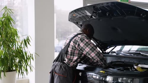 Mecânico de automóveis trabalhando sob o capô do carro na garagem