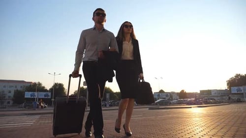 Businessman with His Female Colleague Walking at the City Street and Roll Suitcase on Wheels