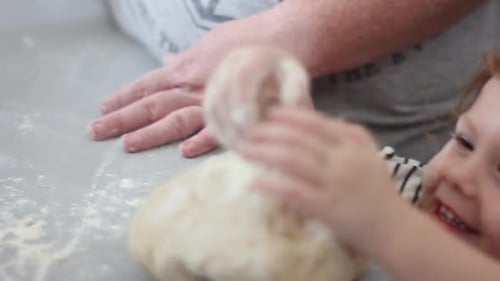 Smiling, happy, pre-schooler girl taking a handful of flour and adding it to the dough while helping