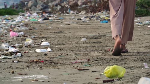 Woman's Feet Walking On Environmentally Polluted Dirty Beach With Garbage Trash. Ecological problem.