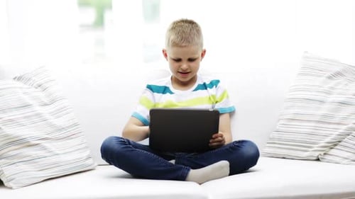 Boy Sitting Cross-Legged Using Tablet on White Sofa