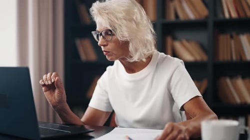 Senior Woman Freelancer Works on Laptop Mature Gray Haired Female in Glasses Working at Home Office