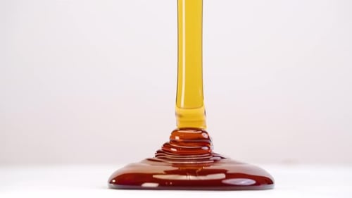 Glob of honey drizzled onto white plate stacking ripples in slow motion back and forth on white stud
