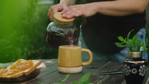 Outdoor Tea Party Woman Pouring Red Hibiscus Tea Into Mug on Wooden Table
