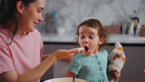 Smiling Woman Giving Child Food in Bright Kitchen