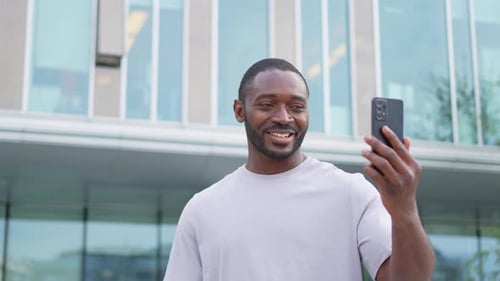 African American Man Holding Smartphone Having Video Chat on Urban Street in City Guy Blogger
