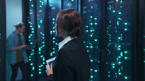 A Woman with a Tablet and Two Men Collaborate in a Server Room