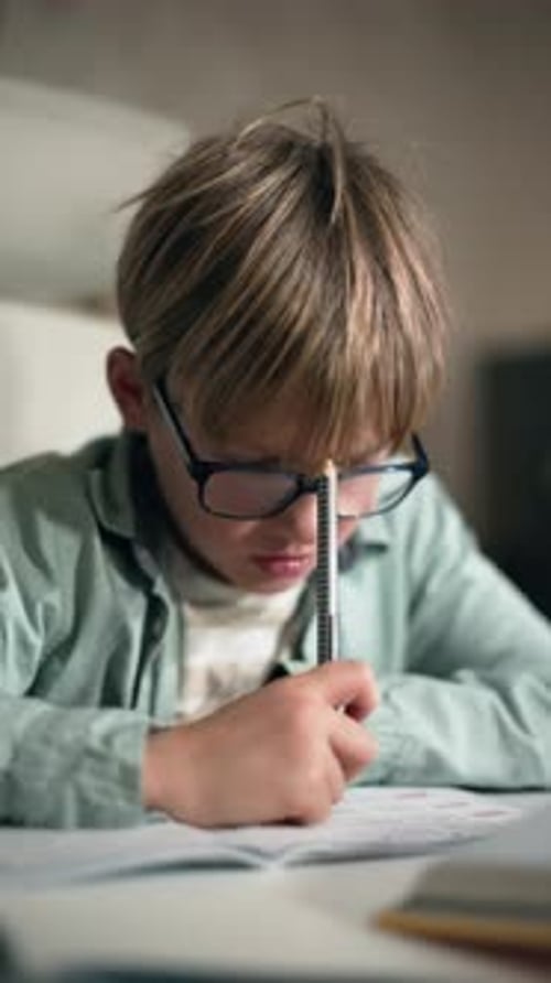 Ein Schuljunge mit Brille denkt bei seinen Hausaufgaben am Tisch zu Hause darüber nach
