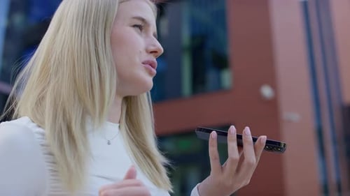 Smiling Woman using Voice Assistant Outside Modern Building