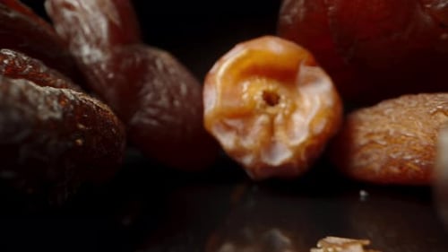Dates and dried apricots are scattered on the table on a black background. Dolly Slider macro