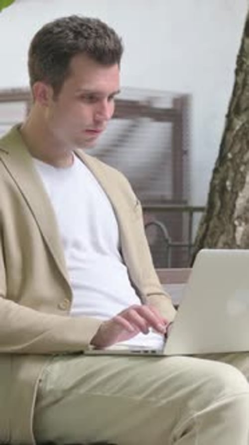 Excited Young Man Using Laptop Outdoors on Bench