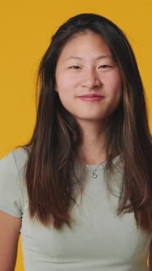 Young woman looking at camera showing thumbs up isolated on yellow background in studio