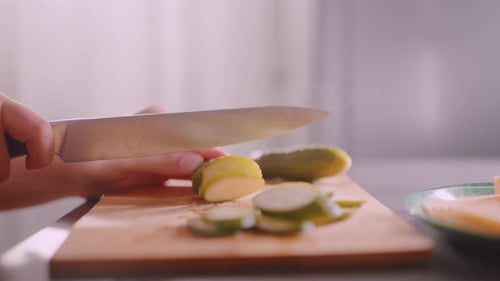 Close Up Person Slicing Cucumber Beside Bread on Plate