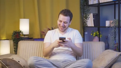 Young Adult Laughing while Using Phone on Sofa