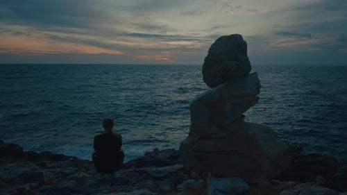 Silhouette of the Man Sitting on the Rocky Coast with a Sea View