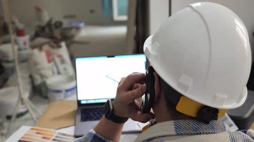 an Engineer is Talking on the Phone and Looking at a Drawing on a Laptop