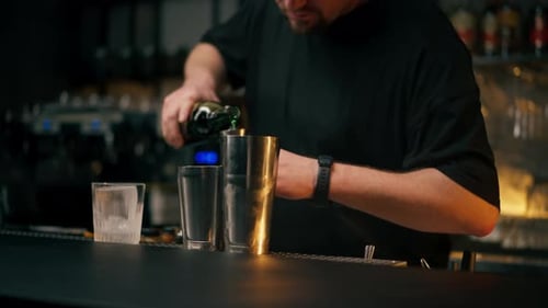Un barman masculin tient une bouteille et verse magistralement la boisson dans un doseur en acier