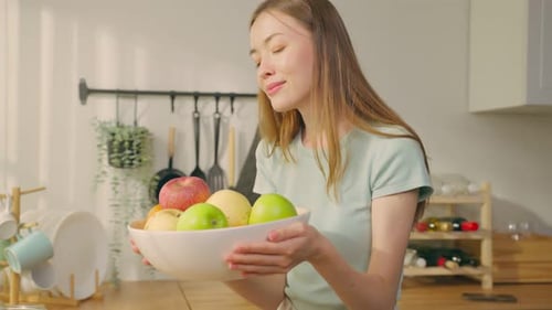 Woman Smells Fruit in Kitchen with a Smile