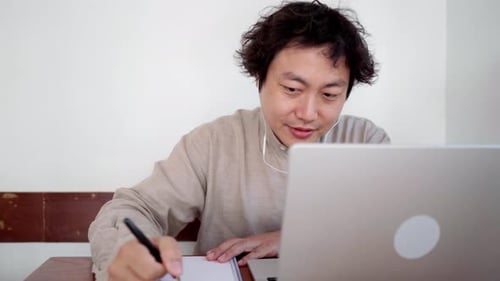Adult man sit and take note for online studying with laptop in cafe during daytime