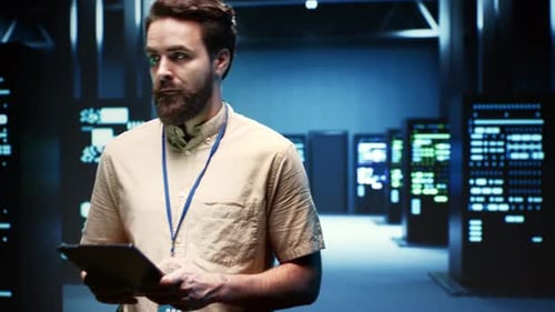 Man Working in a Dark Server Room with Tablet