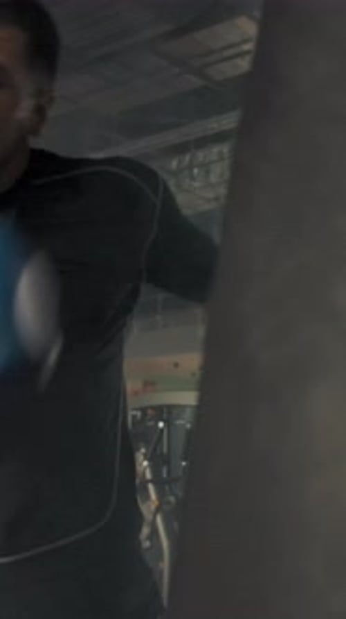 Vertical of Side View of Young Caucasian Athlete Wearing Punching Punching Bag in Modern Gym