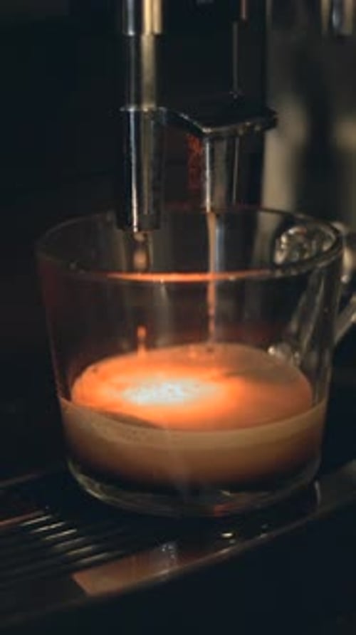 Coffee From Espresso Machine Dripping Into Clear Cup Preparing Coffee In The Office Close Up