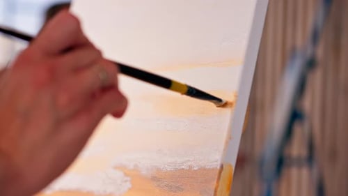 Close-up of a girl artist with a brush applying oil paint to a painting standing on an easel