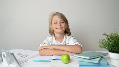 Middle School Smiling Student Boy Sitting at Desk Studying Writing Book Homework and Tablet at Class