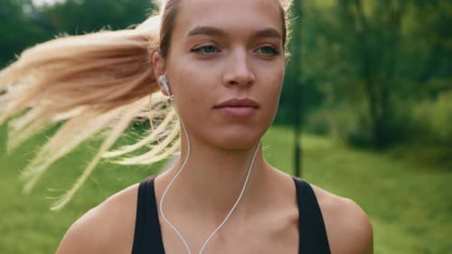Portrait of the Female Running in the Park Wearing Earphones Listening to Music