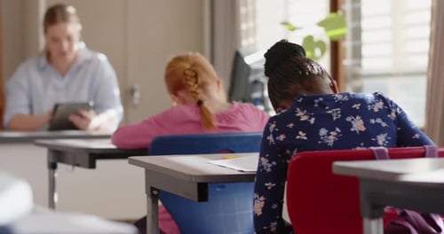 In school, female teacher using tablet while students focusing on classroom activities