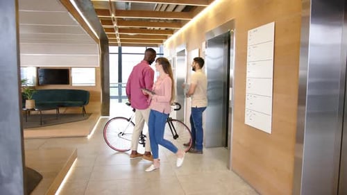 Entering elevator, man with bicycle and diverse colleagues walking in modern office