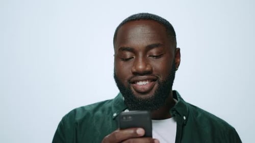 Smiling african american man browsing internet on smartphone in studio portrait
