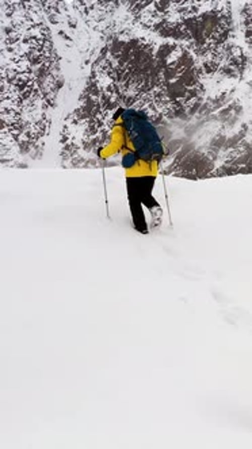 Mountaineer Walking on Snow with Trekking Poles Near Snowy Mountain Range