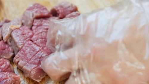 Cutting Raw Meat into Cubes on Wooden Board