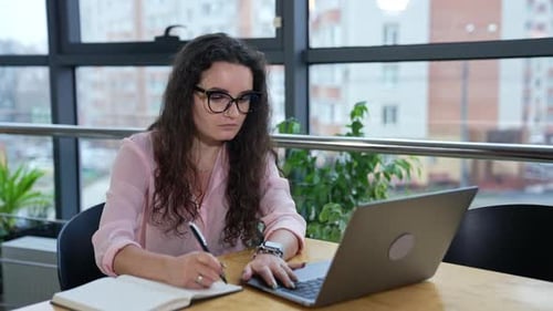 Business lady works with laptop at the table. Working on computer and taking notes.