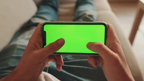 Close-up of the hands of man lying on sofa playing on mobile phone