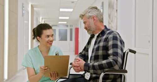 Nurse Assisting WheelchairBound Man in Hospital Corridor