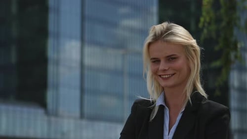 A young corporate employee, a manager, stands in the street confident and looks at the camera. She i