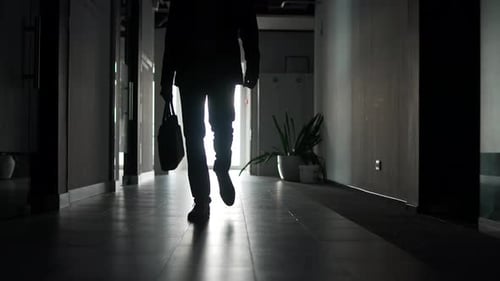 Silhouette of the legs of a businessman in a formal suit walking along corridor of office building.