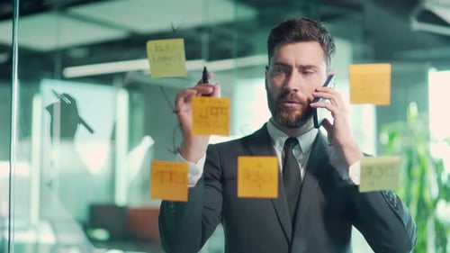 business man talking on the phone in a modern office behind a glass task partition wall with paper